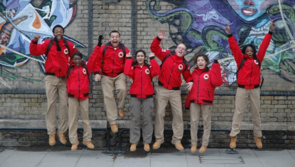 Group of volunteer mentors in red jackets standing against a graffiti wall and cheering