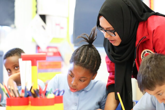 Female volunteer mentor with a hijab leaning over a pupil
