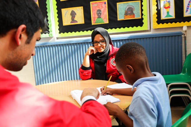 Two volunteer mentors at a table working with a pupil