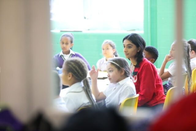 Through the door of a classroom, with a volunteer mentor seated at a table with pupils