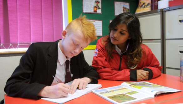 Volunteer mentor working with a pupil with a book open in front of them