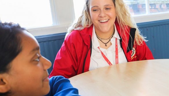 female volunteer sitting at a table with pupil and smiling